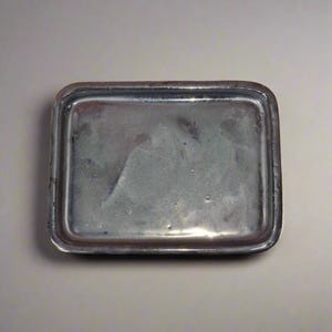 May include: A rectangular ceramic tray with a light blue glaze. The tray has a slightly raised rim and a smooth surface.