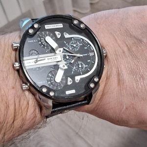 May include: A Diesel watch with a black face and silver casing is displayed. The watch features multiple sub-dials and the text "DIESEL" is visible. The watch is on a black leather band.