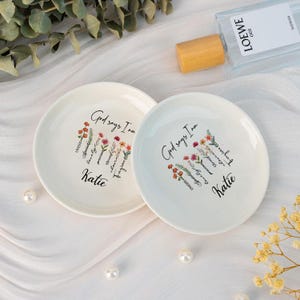 May include: Two white ceramic ring dishes with floral designs and the text "God says I am" with a list of positive affirmations and the name "Katie" on each dish.
