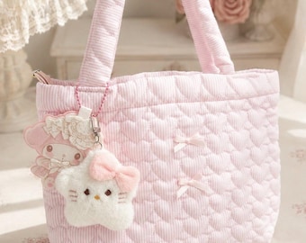 May include: A light pink quilted tote bag featuring a repeating heart pattern and thin white stripes. The bag has two top handles, two small decorative bows on the front, and two plush character charms attached to the side with a beaded chain.