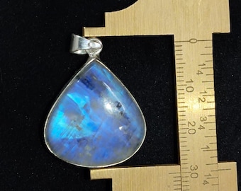 May include: A teardrop-shaped pendant with a silver-colored bezel. The gemstone inside is a vibrant blue with internal patterns. The pendant is being measured with a ruler, showing its size.
