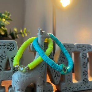 May include: Two colorful bracelets made of small, round beads. One bracelet is bright yellow and the other is turquoise. The bracelets are on a small gray ceramic giraffe figurine.