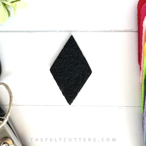 May include: A black felt diamond shape, approximately 2 inches in size, on a white surface. The felt is textured and has a slightly fuzzy appearance.