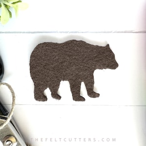 May include: Brown felt bear silhouette cutout. The bear is standing on a white surface.