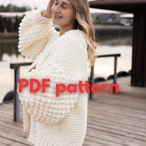 Könnte beinhalten: Cremefarbene, grob gestrickte Strickjacke mit weiten Ärmeln. Der Text "PDF pattern" ist rot über das Bild gelegt. Die Strickjacke wirkt weich und warm, passend für kühleres Wetter.