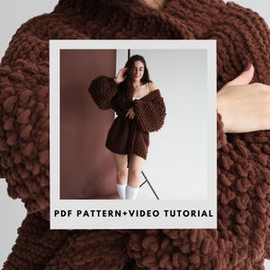 May include: A dark brown, oversized knitted cardigan with voluminous sleeves. The cardigan is worn open, showing a white top and shorts. The image includes the text "PDF PATTERN+VIDEO TUTORIAL" in white letters at the bottom of the image.