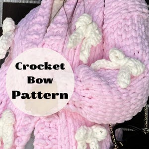May include: A light pink crocheted garment with white bow accents. The garment has a soft, textured appearance. The text "Crochet Bow Pattern" is displayed in a circular graphic.