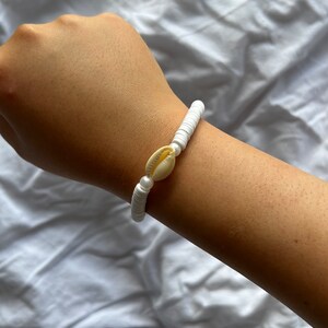 Peut inclure: Bracelet en perles de coquillages blanches avec un seul charme de coquillage plus grand.