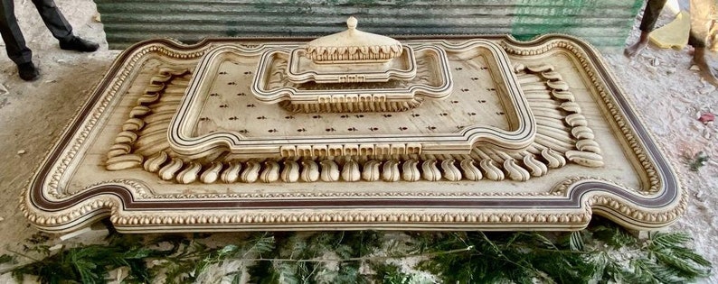 May include: A large, intricately carved wooden tray with a raised, ornate centre piece. The tray is decorated with a repeating pattern of scrolls and leaves, and the centre piece features a dome-shaped design.