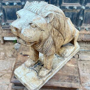 Puede incluir: Una estatua de le&oacute;n de piedra tallada con un acabado blanco desgastado. El le&oacute;n est&aacute; de pie sobre una base rectangular y tiene una melena y una cara detalladas.
