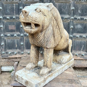 Puede incluir: Una escultura de piedra tallada a mano, detallada, de un le&oacute;n con un acabado beige desgastado. El le&oacute;n est&aacute; sentado sobre una base rectangular y tiene una expresi&oacute;n feroz.