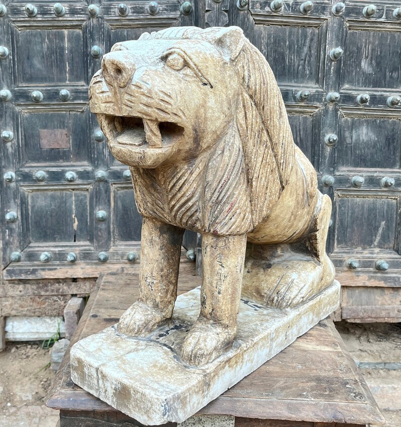 Puede incluir: Una escultura de piedra tallada a mano, detallada, de un le&oacute;n con un acabado beige desgastado. El le&oacute;n est&aacute; sentado sobre una base rectangular y tiene una expresi&oacute;n feroz.