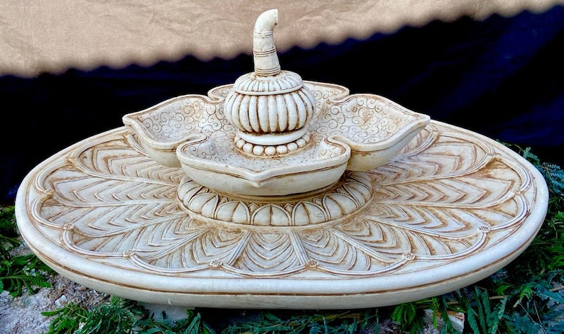 May include: A white ceramic fountain with a lotus flower design. The fountain has three tiers and a central spout. The fountain is decorated with intricate carvings.