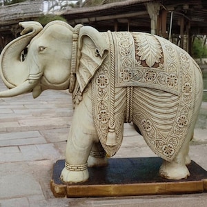 Puede incluir: Una estatua de elefante tallada en blanco con intrincados detalles en su espalda y trompa. La estatua est&aacute; de pie sobre una base de madera.