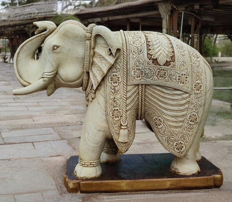 Puede incluir: Una estatua de elefante tallada en blanco con intrincados detalles en su espalda y trompa. La estatua est&aacute; de pie sobre una base de madera.