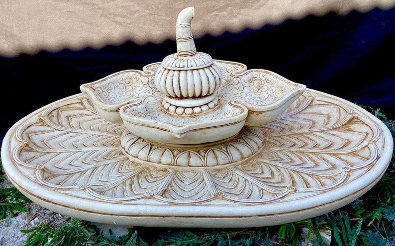 May include: A white ceramic fountain with a lotus flower design. The fountain has three tiers, each with a bowl-shaped basin. The top tier features a decorative finial.