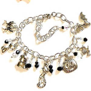 May include: Silver charm bracelet with Halloween-themed charms. Charms include a spider, cat, ghost, pumpkin, bat, and witch's broom. Black beads and clear crystals are also attached to the bracelet.