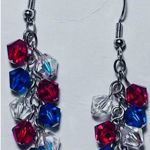May include: Dangling earrings with a patriotic theme. Each earring features a silver-tone hook and chain, adorned with clusters of red, white, and blue faceted beads. The beads are arranged in a cascading design.