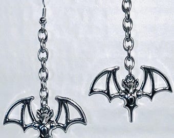 May include: A pair of silver dangle earrings featuring a bat design. Each earring has a silver chain and a bat charm with spread wings.