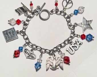 Puede incluir: Una pulsera de dijes patriótica con dijes plateados y cuentas rojas, blancas y azules. Los dijes incluyen una bandera, una estrella, un águila, un signo de la paz y la palabra "USA". La pulsera también tiene las palabras "God Bless America" y "Freedom".