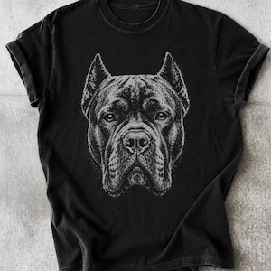 Könnte beinhalten: Ein schwarzes T-Shirt mit kurzen Ärmeln und einer detaillierten weißen grafischen Illustration eines Hundegesichts auf der Brust. Der Hund hat spitze Ohren, eine breite Schnauze und fokussierte Augen, dargestellt in einem skizzenhaften Stil.