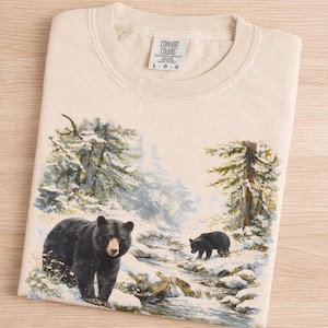 Camiseta vintage de invierno con oso negro - Escena retro de los 90 en un bosque nevado - Camiseta gráfica estilo cabaña gorpcore - Comfort Colors 1717 Unisex