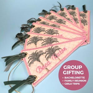 May include: A collection of quilted, diamond-patterned tags with a pink border and embroidered palm trees. The tags have the text "Boca Raton" in pink script and are adorned with green velvet ribbon and gold-colored metal rings. The image also includes a pink circle with the text "GROUP GIFTING".