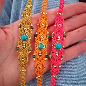 May include: Three macrame bracelets in gold, orange, and pink. Each bracelet features a central turquoise stone, accented with gold beads and smaller green stones. The bracelets are displayed on a denim background.