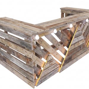 May include: An L-shaped bar counter constructed from reclaimed wooden pallets with a natural weathered finish. The front features a geometric mountain-inspired pattern with integrated warm LED strip lighting and visible EPAL and HT stamps.