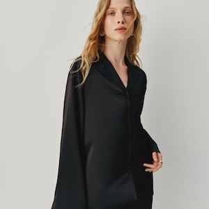 Black 3-piece satin pajama set for women. The set includes a loose-fit satin shirt with fabric-covered buttons, a carefully crafted bra with a secure metal clasp, and oversized pants with an elastic waistband and adjustable belt for a customizable fit. The pants can be worn on the waist or hips, offering both comfort and elegance.