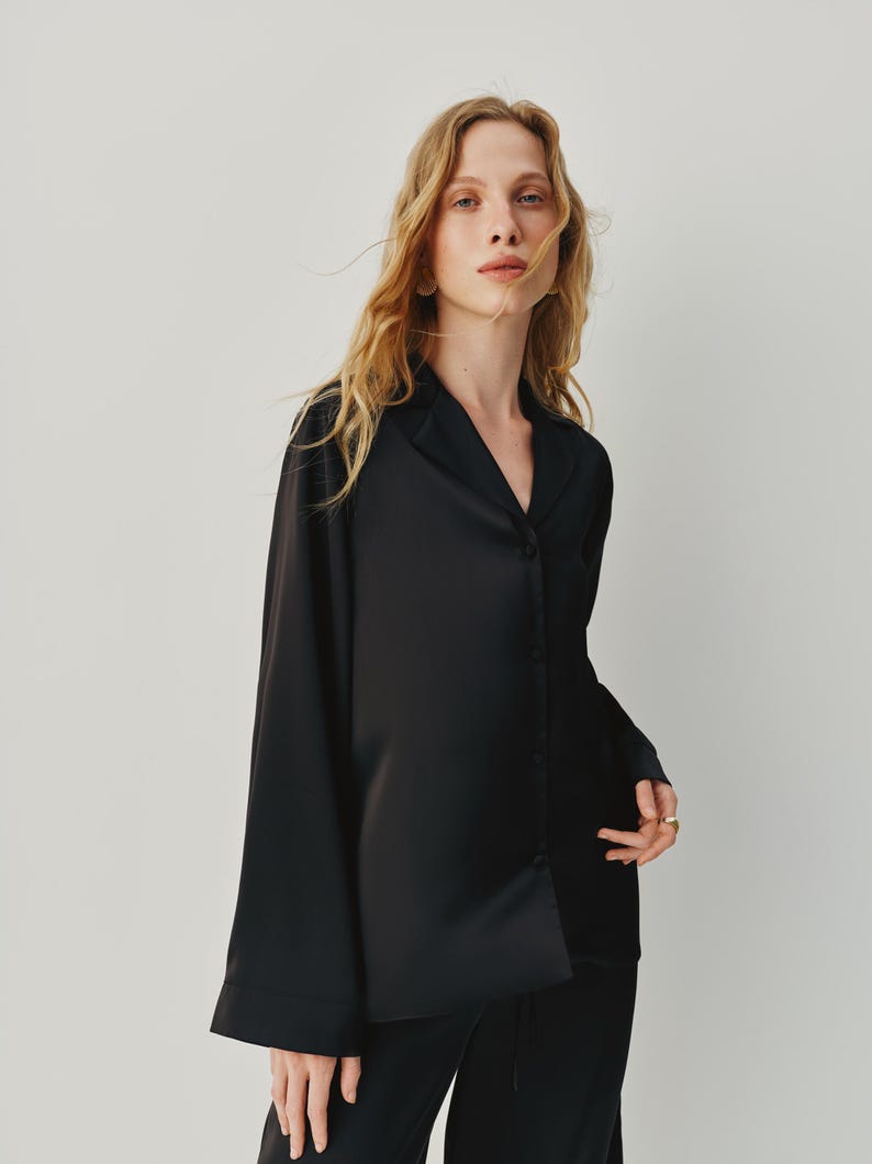 Black 3-piece satin pajama set for women. The set includes a loose-fit satin shirt with fabric-covered buttons, a carefully crafted bra with a secure metal clasp, and oversized pants with an elastic waistband and adjustable belt for a customizable fit. The pants can be worn on the waist or hips, offering both comfort and elegance.