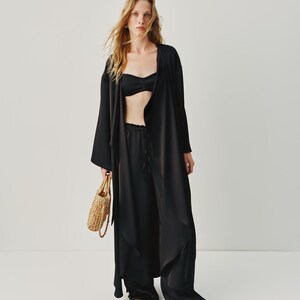 Elegant 3-piece black silk suit with a loose-fitting cape, slits, and a belt, which can be worn as a standalone dress. The top features hand-glued pieces and a metal zipper, while the relaxed-fit pants have an elastic waistband and adjustable belt for a customizable fit. Ideal for a chic bridal set or summer pantsuit.