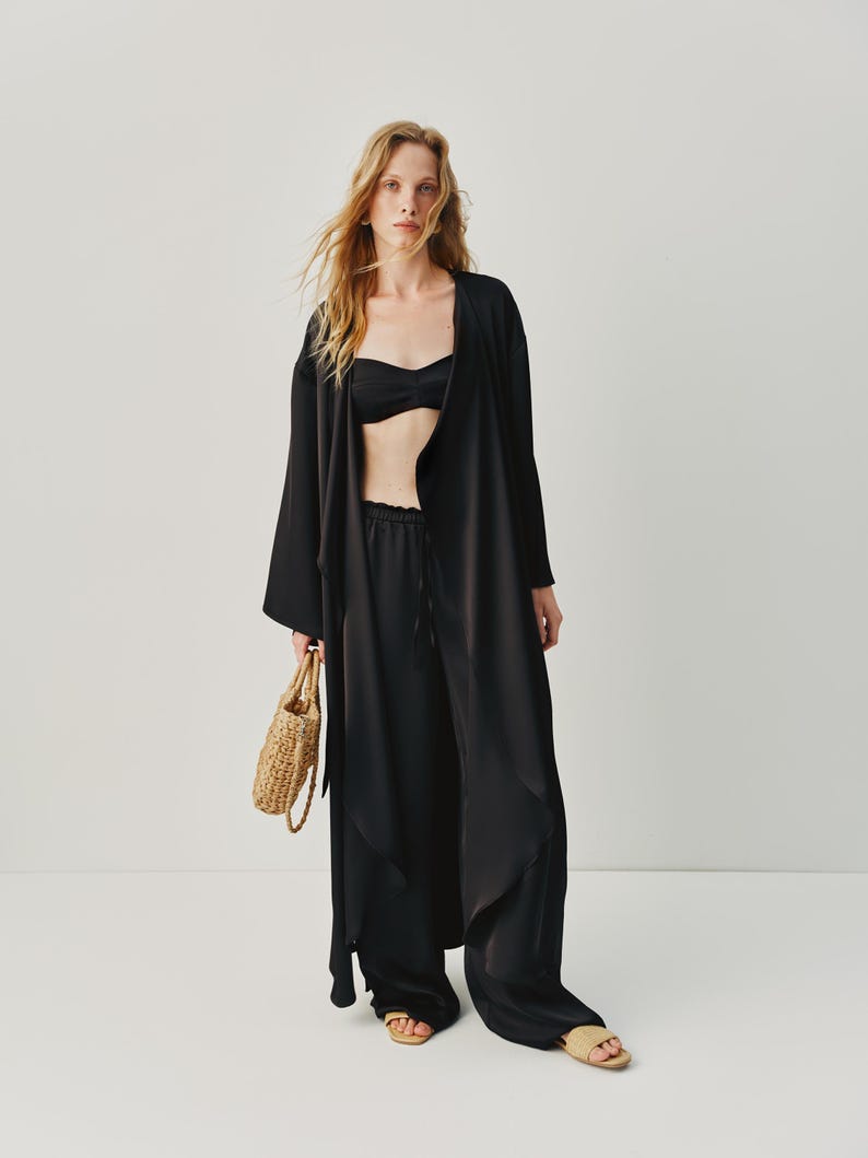 Elegant 3-piece black silk suit with a loose-fitting cape, slits, and a belt, which can be worn as a standalone dress. The top features hand-glued pieces and a metal zipper, while the relaxed-fit pants have an elastic waistband and adjustable belt for a customizable fit. Ideal for a chic bridal set or summer pantsuit.