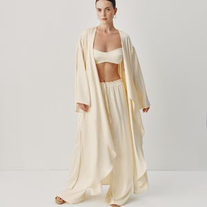 May include: A white long-sleeved robe with a draped design and wide-leg pants. The robe has a relaxed fit and a shawl collar. The pants have a drawstring waist and a wide leg.