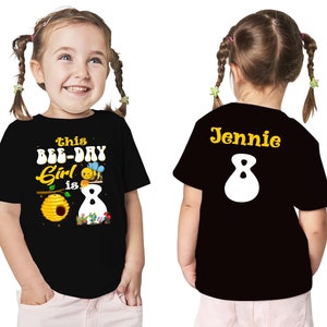 May include: Black t-shirt with a bee and honeycomb design and the text "This Bee-Day Girl is 8". The back of the shirt has the name "Jennie" and the number "8" in yellow.