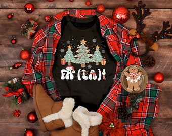 May include: A black t-shirt with a Christmas tree design and the text "Fa La La" in a retro font. The shirt is surrounded by Christmas decorations, including a plaid shirt, ornaments, and a gingerbread man.