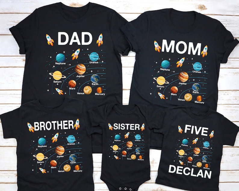 以下が含まれることがあります： 宇宙をテーマにした黒いTシャツ5枚セット。Tシャツには、惑星とロケットのグラフィックが描かれており、「DAD」、「MOM」、「BROTHER」、「SISTER」、「FIVE DECLAN」の文字が書かれています。