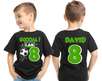 May include: Two black t-shirts with green text and graphics. One shirt says "GOOOAL! I AM 8" with a soccer ball graphic. The other shirt says "DAVID 8".