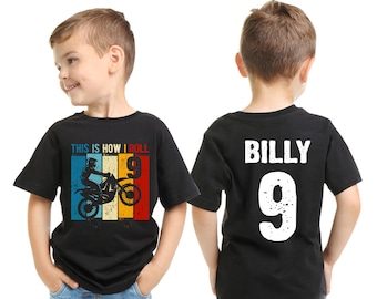 Peut inclure: Deux t-shirts noirs pour enfants. Un t-shirt présente une illustration vintage d'un pilote de motocross et le texte "This is how I roll 9". L'autre t-shirt porte le nom "Billy" et le numéro "9" en blanc.