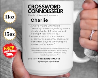 Könnte beinhalten: Eine weiße Keramiktasse mit einem schwarz-weißen Design. Die Tasse zeigt den Text "Crossword Connoisseur" und eine Definition des Begriffs. Die Definition enthält das Wort "Charlie" und beschreibt eine Person, die gerne Kreuzworträtsel löst. Die Tasse ist 11 oz oder 15 oz.