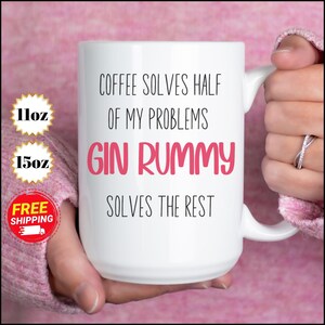 Może przedstawiać: Biały ceramiczny kubek z napisem "COFFEE SOLVES HALF OF MY PROBLEMS, GIN RUMMY SOLVES THE REST" w kolorze czarnym i różowym. Kubek jest trzymany przez osobę. Dostępny w rozmiarach 312 ml i 425 ml.