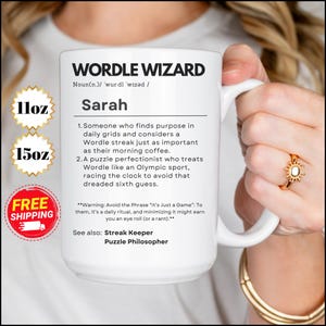 Puede incluir: Taza de cerámica blanca con un diseño en blanco y negro que define a un "Wordle Wizard" como alguien que encuentra propósito en las cuadrículas diarias y considera una racha de Wordle tan importante como su café de la mañana. La taza tiene un asa negra y el texto "11oz" y "15oz" está impreso en la taza.