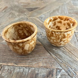 Pode incluir: Duas tigelas de cerâmica marrom e branca com um esmalte manchado. As tigelas estão sobre uma superfície de madeira.
