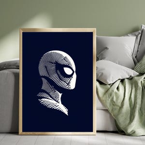 May include: A framed art print showing a white, stylized illustration of Spider-Man's profile on a dark blue backdrop. The artwork has a minimalist design with bold lines, creating a striking contrast. The frame is a light wood colour.