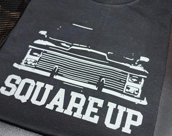 Puede incluir: Camiseta negra con un gráfico blanco de un camión vintage y el texto "SQUARE UP".