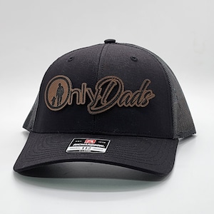 May include: Black and gray trucker hat with a brown leather patch that says "Only Dads" with a silhouette of a father and child.