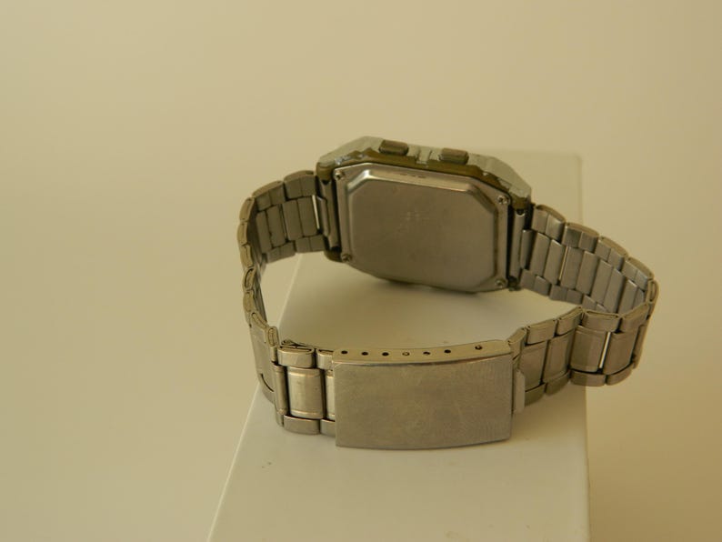 May include: A silver digital wristwatch with a square face and a metal band.