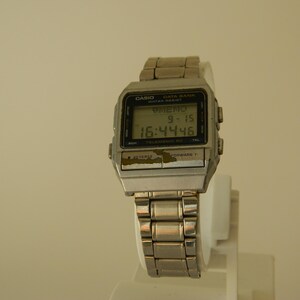 May include: A silver Casio Data Bank watch with a black digital display showing the time 16:44:46 and the date 9-15. The watch has a silver metal band.