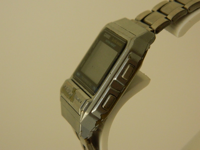 May include: A silver Casio digital watch with a rectangular face and a metal band. The watch has a digital display and several buttons on the side.