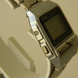 May include: A silver Casio Data Bank watch with a black digital display. The watch has a silver metal band and a black face with white lettering. The watch is in good condition, but shows signs of wear.
